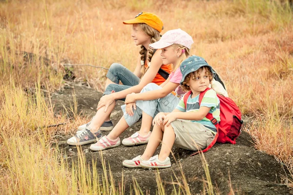 Three little kids with backpack sitting on the footpath in the m — Stock Photo, Image