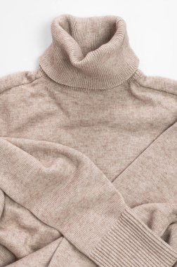 Bej kazak, balıkçı yaka, açık gri arka plan manzaralı yüksek yakalı kazak. Kıyafet konsepti, moda, tarz. Marka reklamı için süveter yaka. Unisex kazağı.