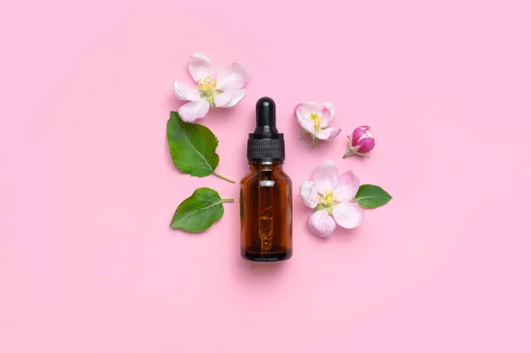 Clean brown glass cosmetic bottles with dropper, delicate spring flowers on pink background flat lay top view. Spring concept of natural organic cosmetics, beauty herbal product spa aroma oil. Mockup.