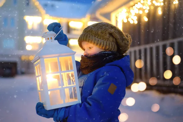 小さな子供はクリスマス前夜の雪の中 小さな町の通りでサンタクロースを待っています 男の子はロウソクを灯して大きな提灯を持っている 魔法と贈り物の赤ちゃんの希望 冬の休日の伝統 — ストック写真