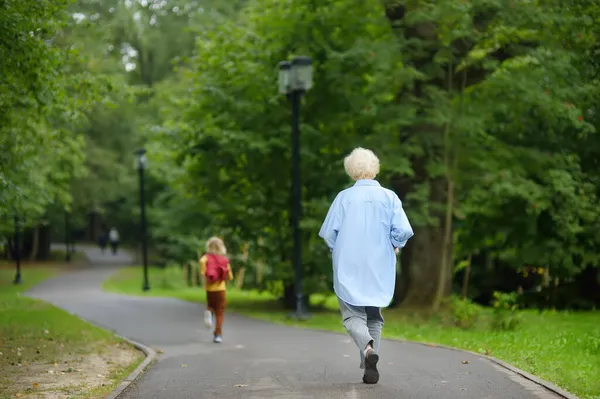 小さな男の子は夏の公園でベビーシッターから逃げます おばあちゃんは子供に追いつこうとしている おばあちゃんと孫 家族における困難な関係 — ストック写真