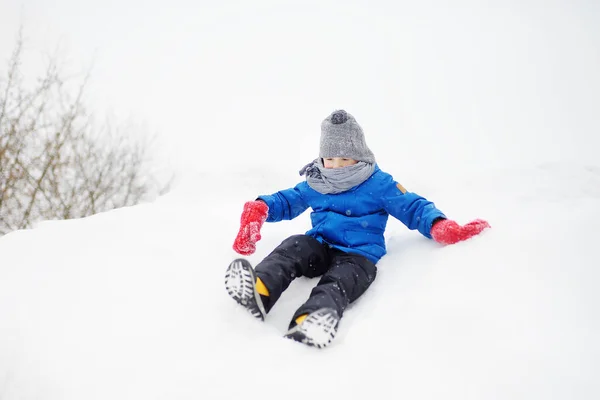 小さな男の子は雪の日に氷のスライドに乗るのを楽しむ 吹雪の中で楽しい赤ちゃん 子供連れの家族のための屋外冬の活動 — ストック写真