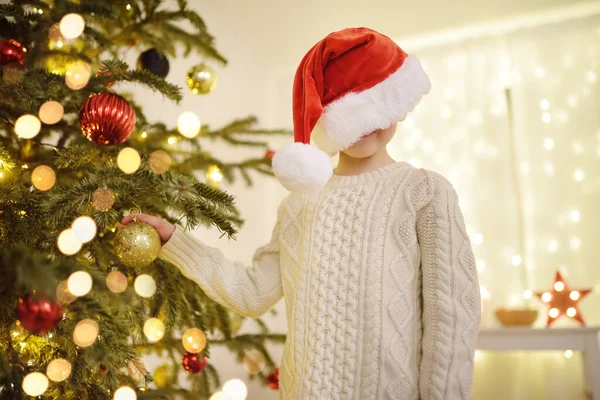 小顽皮的男孩戴着圣诞老人的帽子 正准备庆祝圣诞节 可爱的孩子用玻璃玩具装饰圣诞树 在新年的夜晚 婴儿对魔法和礼物的希望 寒假前后的传统 — 图库照片
