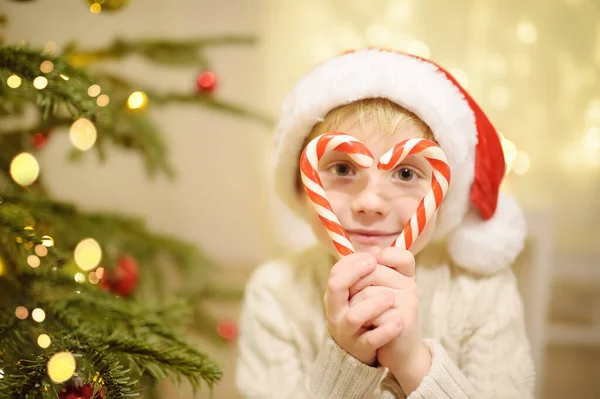 小男孩戴着圣诞礼帽 准备庆祝圣诞节 可爱的孩子用糖果装饰圣诞树 婴儿透过心形的糖果看过去 寒假前后的传统 — 图库照片