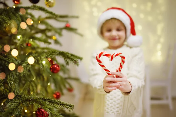 小男孩戴着圣诞礼帽 准备庆祝圣诞节 可爱的孩子用糖果装饰圣诞树 婴儿把糖果保持在心形 寒假前后的传统 — 图库照片