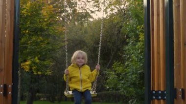 Küçük çocuk sonbahar günü halk parkında salıncakta sallanırken eğleniyor. Mutlu çocuk sallanmaktan zevk alır. Şehirde çocuk için aktif açık hava eğlencesi