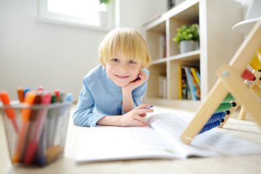 İlkokul öğrencisi evde ödev yapıyor. Çocuk saymayı öğreniyor, aritmetik örnekler çözüyor, çalışma kitabı alıştırmaları yapıyor. Matematik dersi. Anaokulu bebeğini okula hazırlamak. Çocuklar için eğitim.