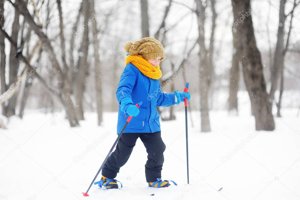 Cute little boy is learning ski during walk in the winter forest. Outdoor activities for children in winter. Kids equipment for winter sports. Physical education lessons. Quality sportswear.