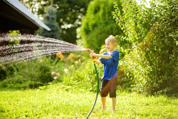 日当たりの良い裏庭で庭のホースで遊んで面白い男の子 水のスプレーで楽しんでいる未就学児 子供連れの家族のための夏の屋外活動 — ストック写真