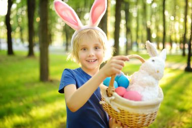Paskalya günü bahar bahçesinde yumurta arayan tavşan kulaklı bir çocuk. Geleneksel festival açık havada. Çocuk Paskalya bayramını kutluyor.