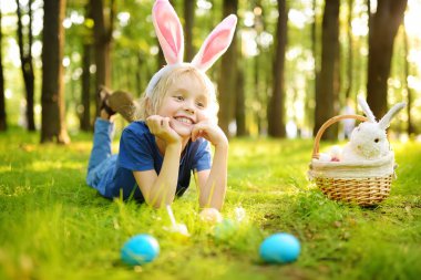 Paskalya günü bahar bahçesinde yumurta arayan tavşan kulaklı bir çocuk. Geleneksel festival açık havada. Çocuk Paskalya bayramını kutluyor.