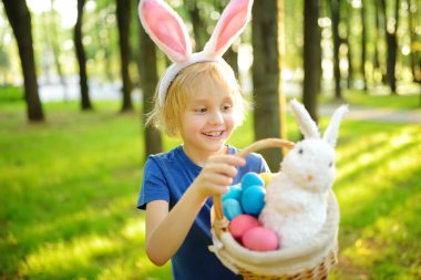 Paskalya günü bahar bahçesinde yumurta arayan tavşan kulaklı bir çocuk. Geleneksel festival açık havada. Çocuk Paskalya bayramını kutluyor.