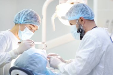 Diş ameliyatı sırasında cerrah ve hemşire. Anestezi yapılmış hasta ameliyathanede. Diş implantı ya da diş çıkarma kliniğine yerleştirilmiş. Ortodonti ameliyatı sırasında genel anestezi..