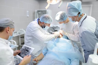 Diş ameliyatı sırasında cerrahlar ve hemşire. Ameliyathanede anestezi edilmiş bir hasta. Kliniğe diş implantı ya da diş çekilmesi yerleştirildi. Ortodonti ameliyatı sırasında genel anestezi.