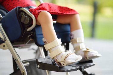 Tekerlekli sandalyede oturan engelli kız. Bacakları ortoza dönmüş. Çocuk serebral felci. Karargahın tedavisi ve rehabilitasyonu. Katılım. Engelli çocuklu bir aile. Özürlü kişi
