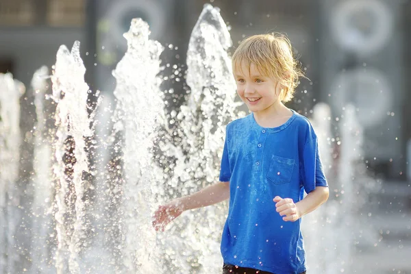 晴れた夏の日には 噴水の水差しの間の広場で小さな男の子が遊んでいます 市内の子供のためのアクティブな夏のレジャー — ストック写真