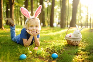 Paskalya günü bahar bahçesinde yumurta arayan tavşan kulaklı bir çocuk. Geleneksel festival açık havada. Çocuk Paskalya bayramını kutluyor.