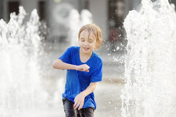 晴れた夏の日には 噴水の水差しの間の広場で小さな男の子が遊んでいます 市内の子供のためのアクティブな夏のレジャー — ストック写真