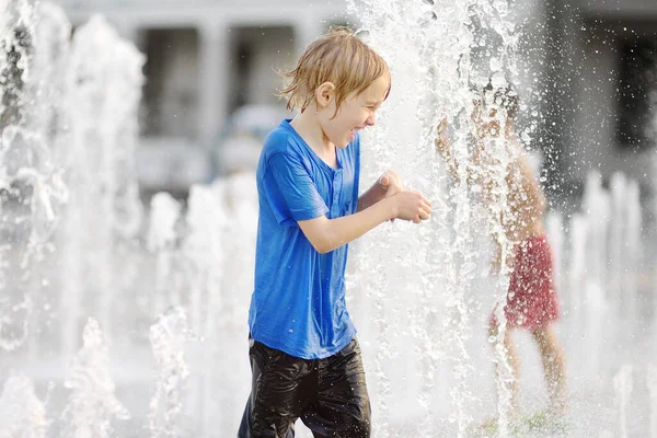 晴れた夏の日には 噴水の水差しの間の広場で小さな男の子が遊んでいます 市内の子供のためのアクティブな夏のレジャー — ストック写真