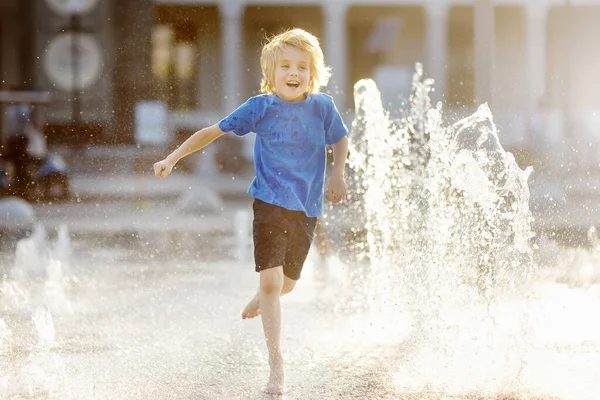 晴れた夏の日には 噴水の水差しの間の広場で小さな男の子が遊んでいます 市内の子供のためのアクティブな夏のレジャー — ストック写真