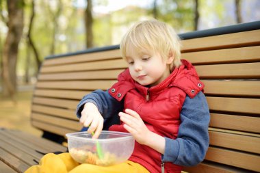 Küçük çocuk öğle yemeğini anaokulundan ya da parktaki plastik konteynırdan yiyor. Sokak çocukları için yiyecek alıyor. Çocuklar için sağlıksız yemekler. Sağlıklı yiyecekler..