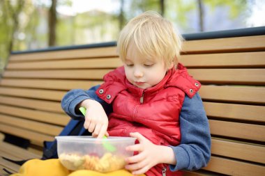 Küçük çocuk öğle yemeğini anaokulundan ya da parktaki plastik konteynırdan yiyor. Sokak çocukları için yiyecek alıyor. Çocuklar için sağlıksız yemekler. Sağlıklı yiyecekler..