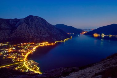 Karadağ 'daki Boka Kotorska' nın mavi saatte deniz manzarası. Kotor körfezi üzerinde Adriyatik deniz manzarası. Deniz kıyısında aydınlık caddeleri ve yolu olan küçük bir kasabanın yukarısına bak. Kartpostal.