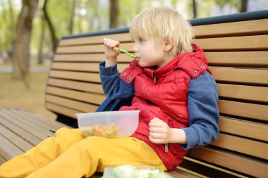 Küçük çocuk öğle yemeğini anaokulundan ya da parktaki plastik konteynırdan yiyor. Sokak çocukları için yiyecek alıyor. Çocuklar için sağlıksız yemekler. Sağlıklı yiyecekler..