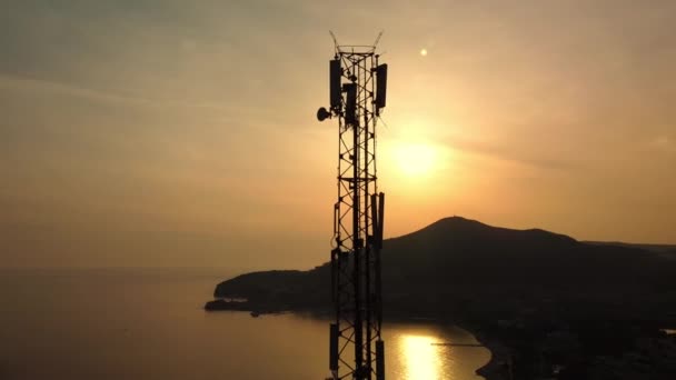 セルタワーのシルエットの驚くべきクローズアップ夕日ドローンビュー 無線接続だ 背景に山や海とセルラータワーの壮大な景色 5Gネットワーク まあサイト — ストック動画