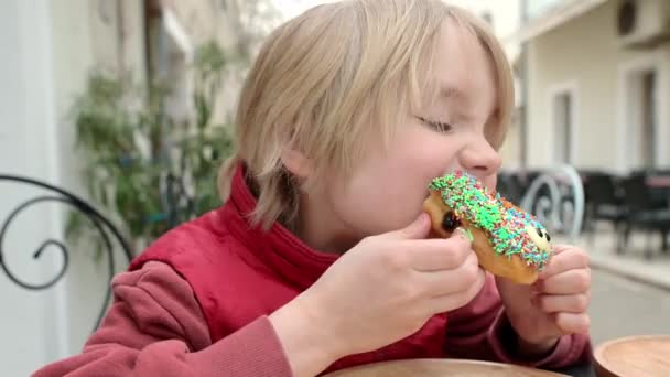 Χαριτωμένο Αγόρι Σχολική Ηλικία Τρώει Αστείο Πολύχρωμο Ντόνατ Ένα Καφέ — Αρχείο Βίντεο