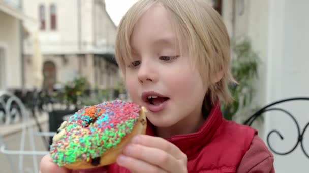Χαριτωμένο Αγόρι Σχολική Ηλικία Τρώει Αστείο Πολύχρωμο Ντόνατ Ένα Καφέ — Αρχείο Βίντεο