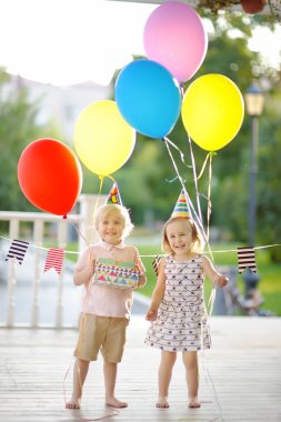 Küçük oğlan ve kız eğleniyor ve renkli balonlarla doğum günü partisini kutluyorlar. Hediyelerle dolu mutlu bir çocuk. Anaokulu öğrencileri ya da yeni yürümeye başlayanlar yaz parkında parti veriyorlar.