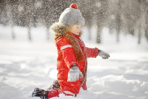 赤い冬の服を着た小さな遊び心のある少年は雪を楽しんでいます 冬に子供たちと積極的な屋外レジャー 暖かい帽子 手の手袋 スカーフの子供は雪の銀行で遊んでいます — ストック写真