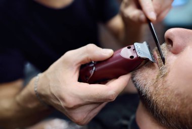 Berber ustası, kuaförde sakallı yakışıklı bir adamı tıraş ediyor. Berber dükkanında saç stili yapan bir kuaför. Profesyonel stilistin hizmetleri. Erkekler için moda saç bakımı. Yakın plan.