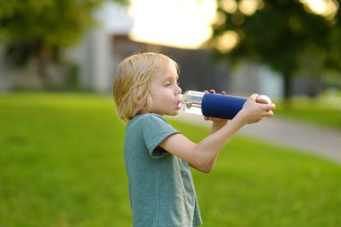 Anaokulu çocuğu, güneşli bir yaz gününde bir bahçede ya da halka açık bir parkta şişeden su içiyor. Susuzluk hissi. Çocuklar için sağlıklı bir yaşam tarzı. Temiz içme suyu bir sağlık kaynağıdır..