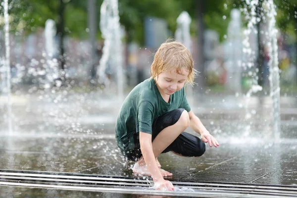晴れた夏の日には噴水のウォータージェットの間の広場で小さな男の子が遊んでいます 大都市の子供たちのためのアクティブな夏のレジャー — ストック写真