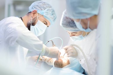 Diş ameliyatı sırasında cerrahlar ve hemşire. Ameliyathanede anestezi edilmiş bir hasta. Kliniğe diş implantı ya da diş çekilmesi yerleştirildi. Ortodonti ameliyatı sırasında genel anestezi.