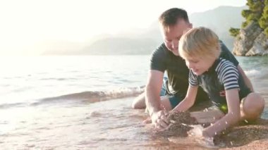 Mutlu çocuk ve olgun babası birlikte kumdan ve taştan bir kale inşa ediyorlar. Neşeli çocuk ve babası deniz kıyısındaki tatillerde eğleniyorlar. Tatillerde aile için deniz kenarında aktif bir eğlence.