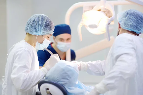 Surgeons and nurse during a dental operation.Anesthetized patient in the operating room.Installation of dental implants or tooth extraction in the clinic. General anesthesia during orthodontic surgery