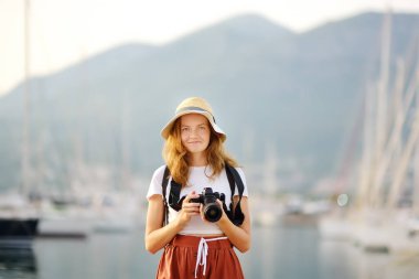 Akdeniz kıyısında fotoğraf çeken çekici genç bir turist kadın. Deniz ve yatların arka planında kamera olan çekici kızıl saçlı kız fotoğrafçı. Turizm ve seyahat kavramı.