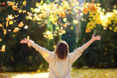 Young woman is having fun while walking through the forest on a sunny autumn day. Girl plays with maple leaves and throws them up. Fallen leaves rustle.