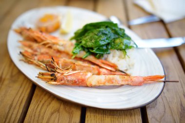 Big grilles shrimps on skewers with rice and spinach on a white plate in restaurant in Cyprus. Dishes of Mediterranean cuisine