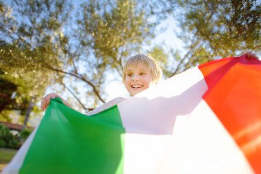 Cute little child holding big Italian flag sunny summer day outdoors. Happy boy celebrate Republic Day second of June. National symbols of Italy.