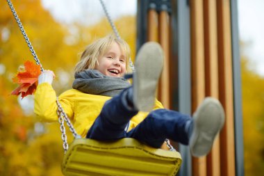 Küçük çocuk sonbahar günü halk parkında salıncakta sallanırken eğleniyor. Mutlu çocuk sallanmaktan zevk alır. Şehirde çocuk için aktif açık hava eğlencesi