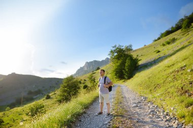 Mature man tourist with backpack and camera is hiking on mountain valley. Person during travel. Tourism and adventure.