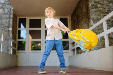 Little student boy with a backpack at the door of school building. Happy child running home after the end of lessons. Kids back to school concept.