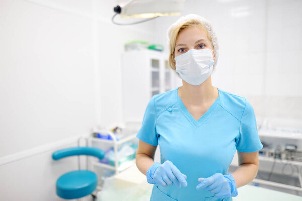 Portrait of female surgeon wearing in medical face mask and protective gloves. Doctor is preparing for surgery in operation room. Medicine and healthcare.