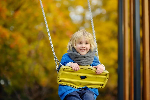 秋の日に公園の遊び場でスイングを楽しんでいる小さな男の子 幸せな子供はスイングをお楽しみください 市内の子供のためのアクティブな屋外レジャー — ストック写真