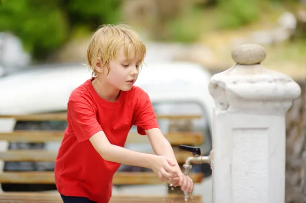 Closeup photo of child washing hands in a city fountain. Little boy drinking clean water from a street pump. Clean drinkable water is a source of health.