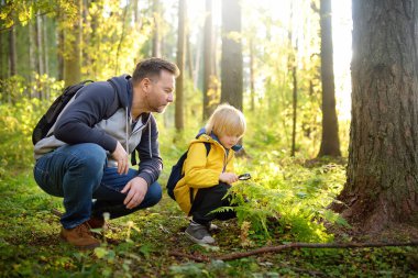 School boy and his father hiking together and exploring nature with magnifying glass. Little boy and dad spend quality family time in sunny forest of second summer. Daddy and little son. Fatherhood.